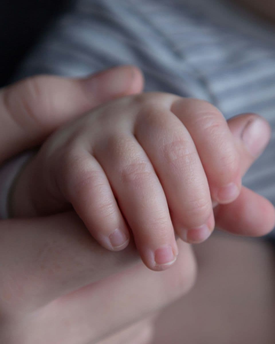 A newborn's hand resting in a parent's hand