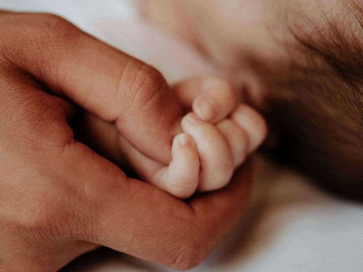 A parent's hand holding a sleeping newborn's hand